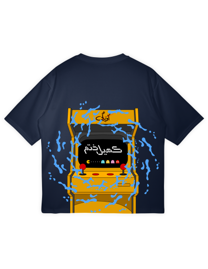 The back of a dark navy blue t-shirt featuring a large yellow arcade cabinet graphic. The screen displays the Urdu text "Khel Khatam" (Game Over) and "Aagay" (Next) with Pac-Man and the ghosts visible. Blue splash effects surround the top of the cabinet.